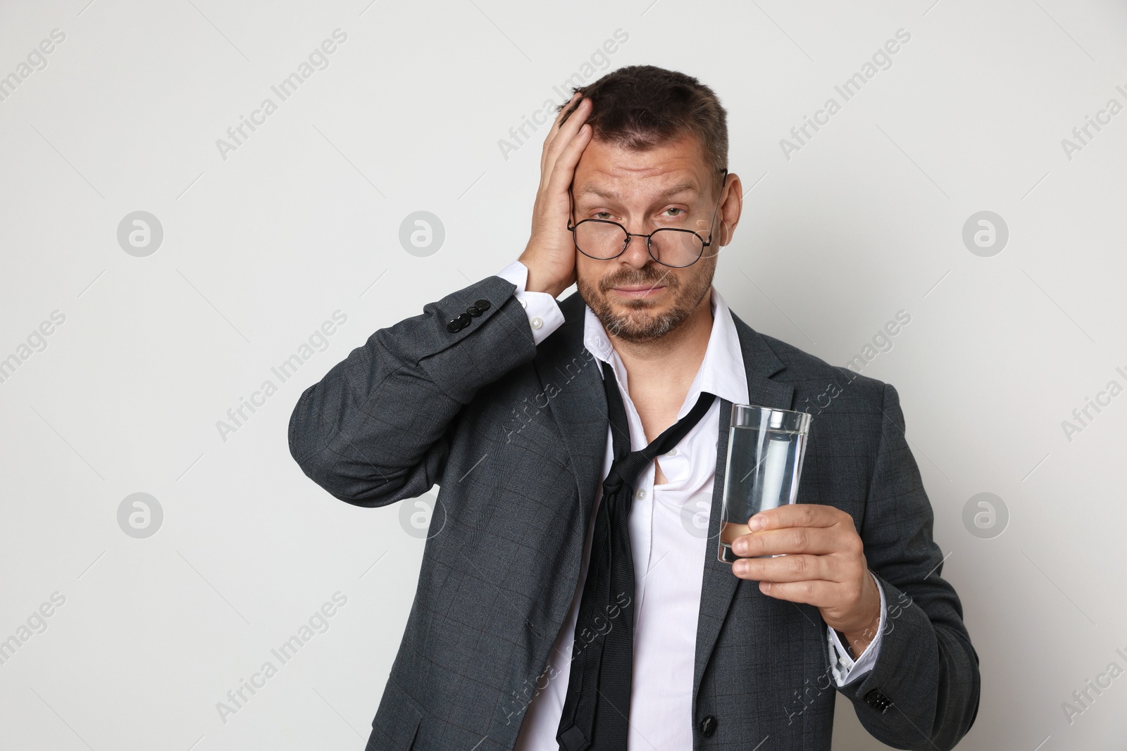Photo of Man with glass of water suffering from hangover on white background