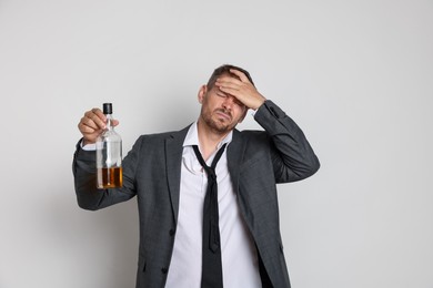 Photo of Man with bottle of whiskey suffering from hangover on white background