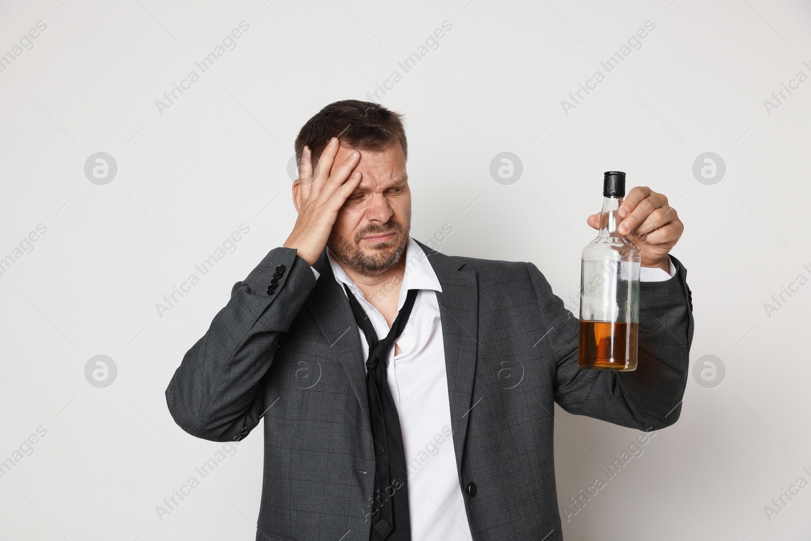 Photo of Man with bottle of whiskey suffering from hangover on white background