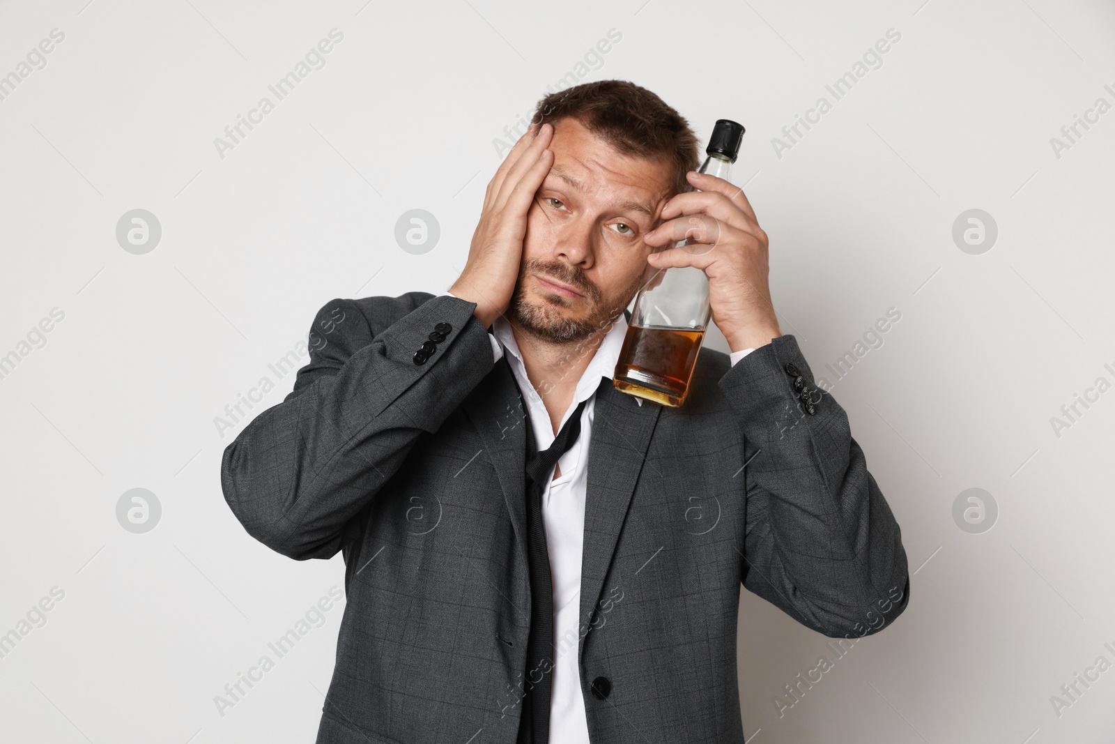 Photo of Man with bottle of whiskey suffering from hangover on white background
