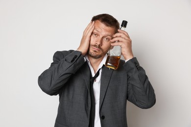 Photo of Man with bottle of whiskey suffering from hangover on white background