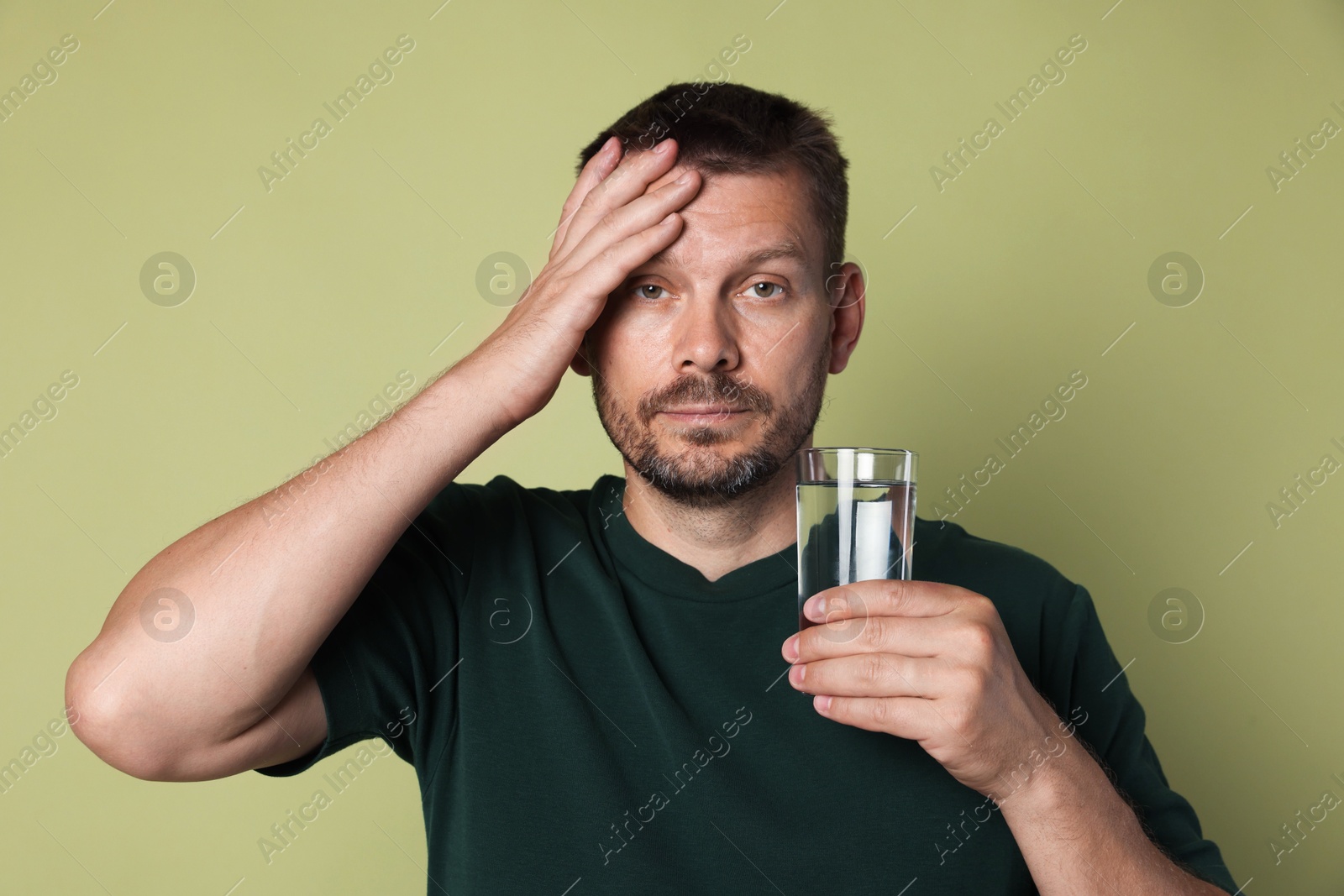 Photo of Man with glass of water suffering from hangover on olive background
