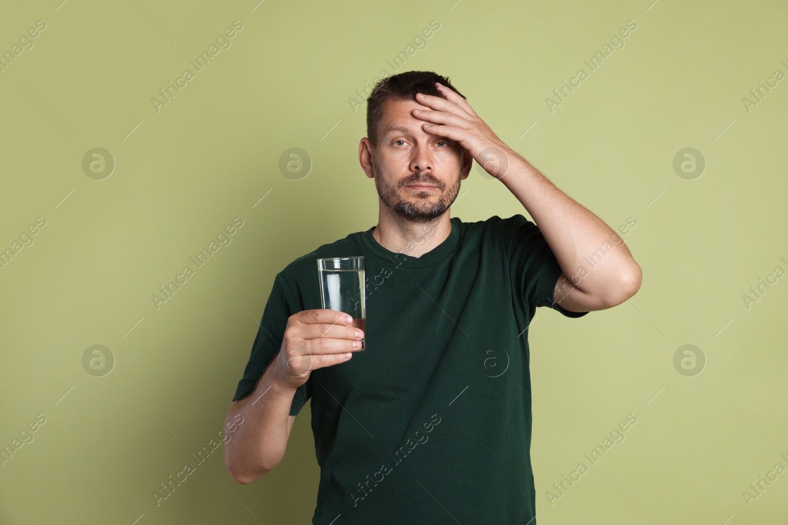 Photo of Man with glass of water suffering from hangover on olive background