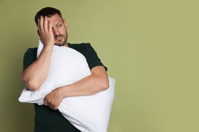 Photo of Man with pillow suffering from hangover on olive background, space for text