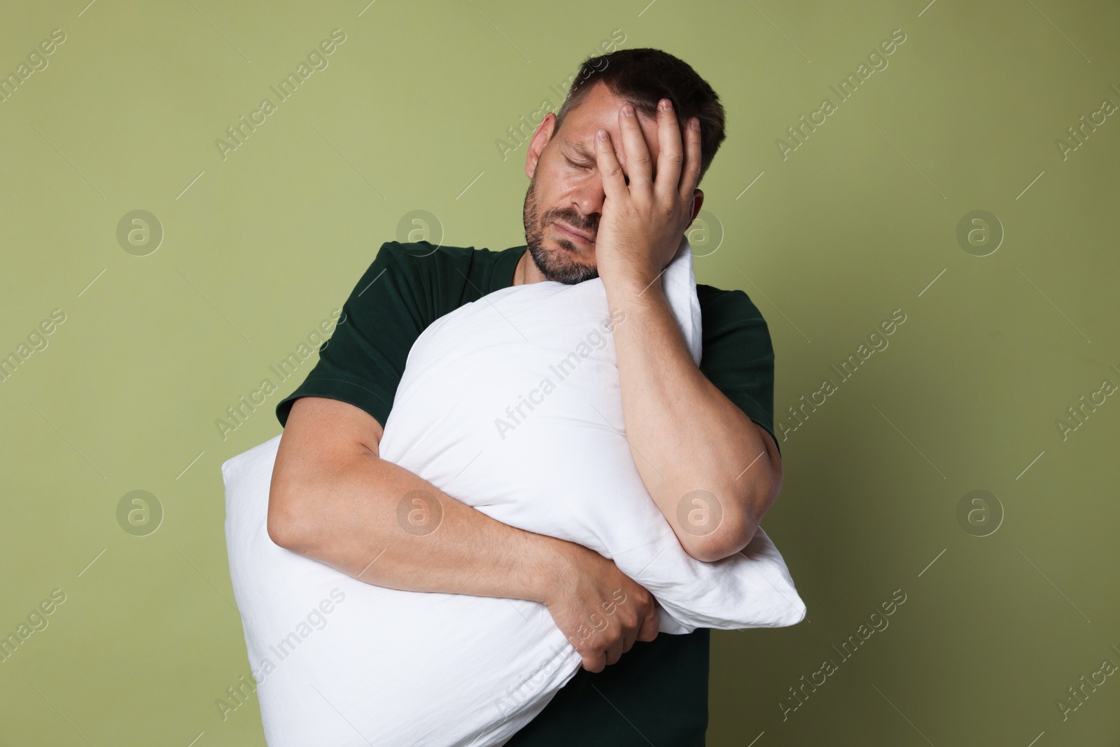 Photo of Man with pillow suffering from hangover on olive background