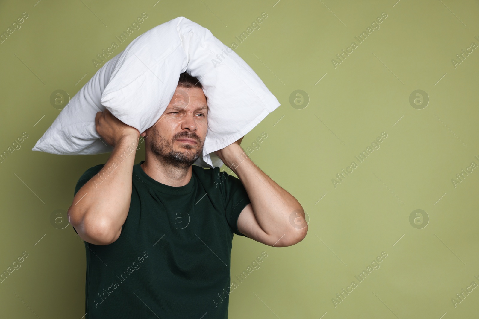 Photo of Man with pillow suffering from hangover on olive background, space for text