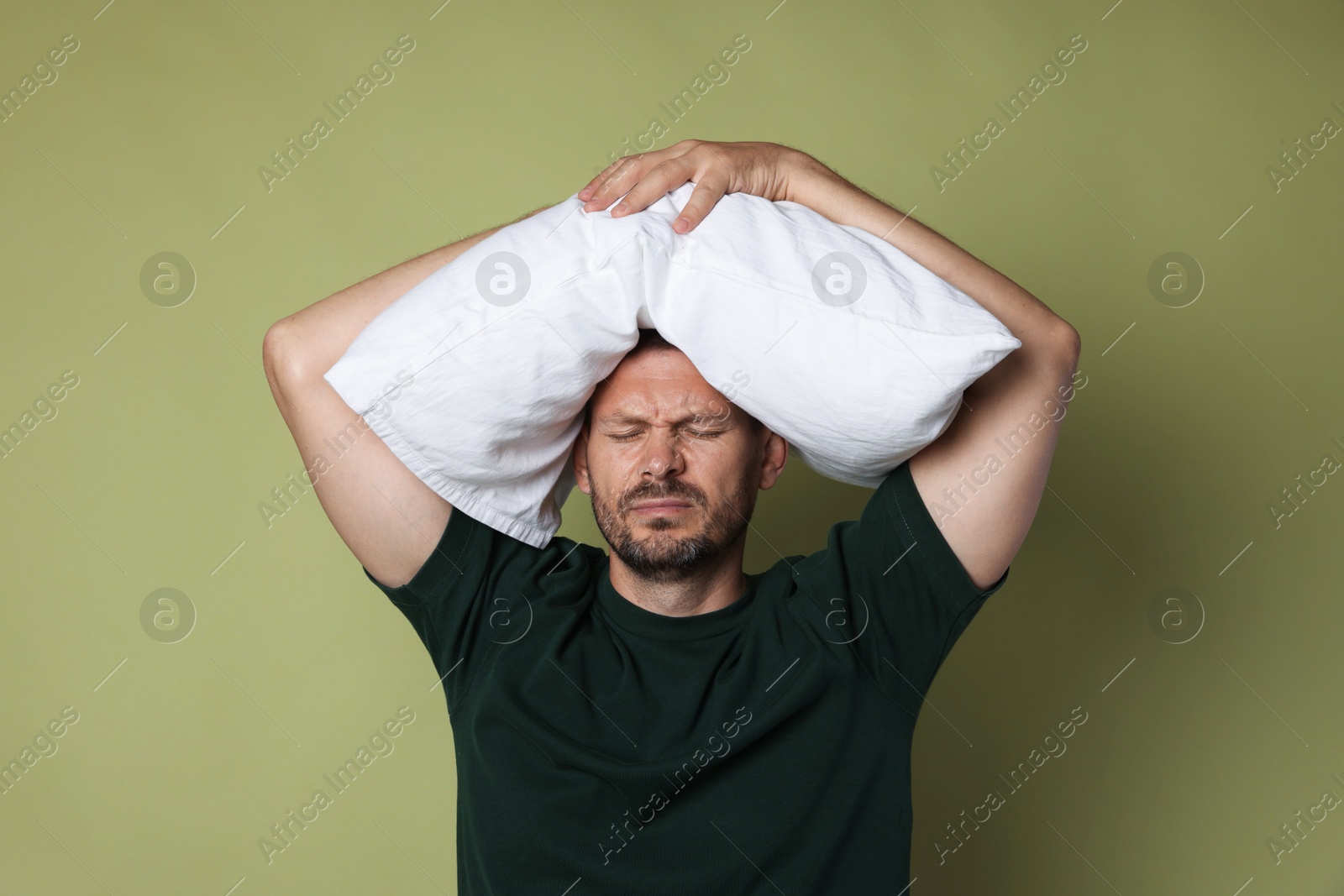 Photo of Man with pillow suffering from hangover on olive background