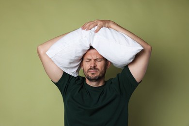 Photo of Man with pillow suffering from hangover on olive background