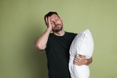 Photo of Man with pillow suffering from hangover on olive background