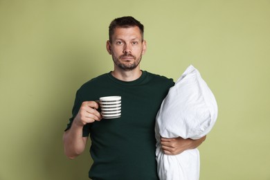 Photo of Man with pillow and cup of drink suffering from hangover on olive background