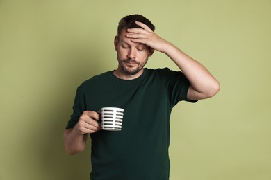 Photo of Man with cup of drink suffering from hangover on olive background