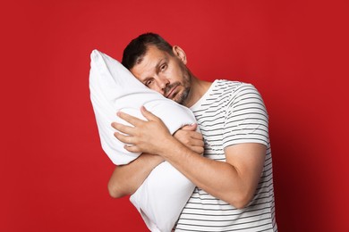 Photo of Man with pillow suffering from hangover on red background