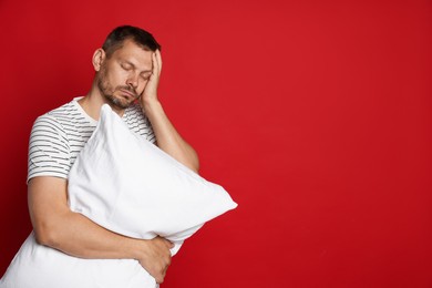 Photo of Man with pillow suffering from hangover on red background, space for text