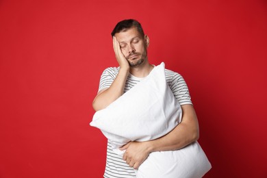 Photo of Man with pillow suffering from hangover on red background