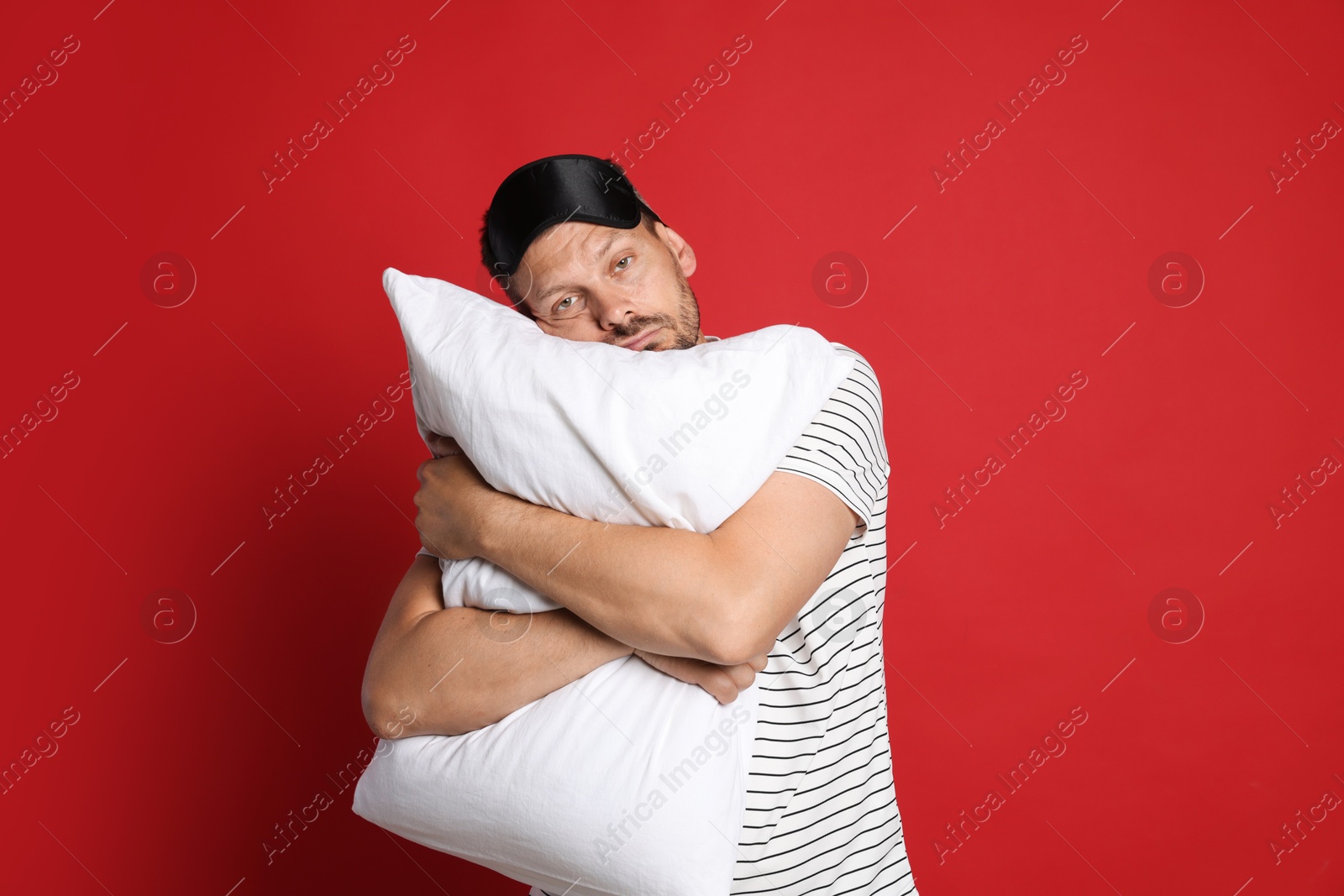 Man with pillow and sleep mask suffering from hangover on red background Photo of Man with pillow and sleep mask suffering from hangover on red background