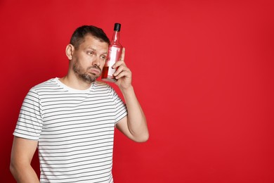 Photo of Man with bottle of whiskey suffering from hangover on red background, space for text
