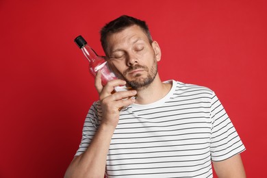 Photo of Man with bottle of whiskey suffering from hangover on red background