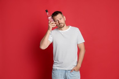Photo of Man with bottle of whiskey suffering from hangover on red background