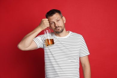 Photo of Man with bottle of whiskey suffering from hangover on red background