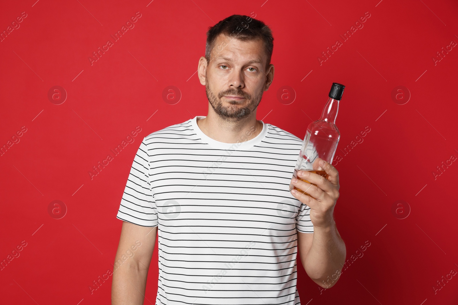 Photo of Man with bottle of whiskey suffering from hangover on red background