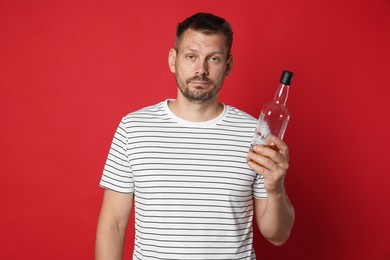 Photo of Man with bottle of whiskey suffering from hangover on red background