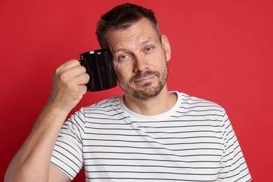 Photo of Man with cup of drink suffering from hangover on red background