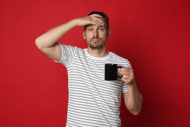 Photo of Man with cup of drink suffering from hangover on red background