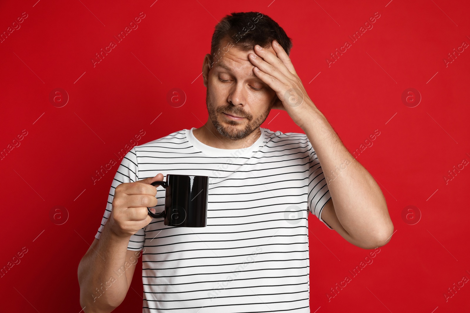 Photo of Man with cup of drink suffering from hangover on red background