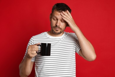 Photo of Man with cup of drink suffering from hangover on red background