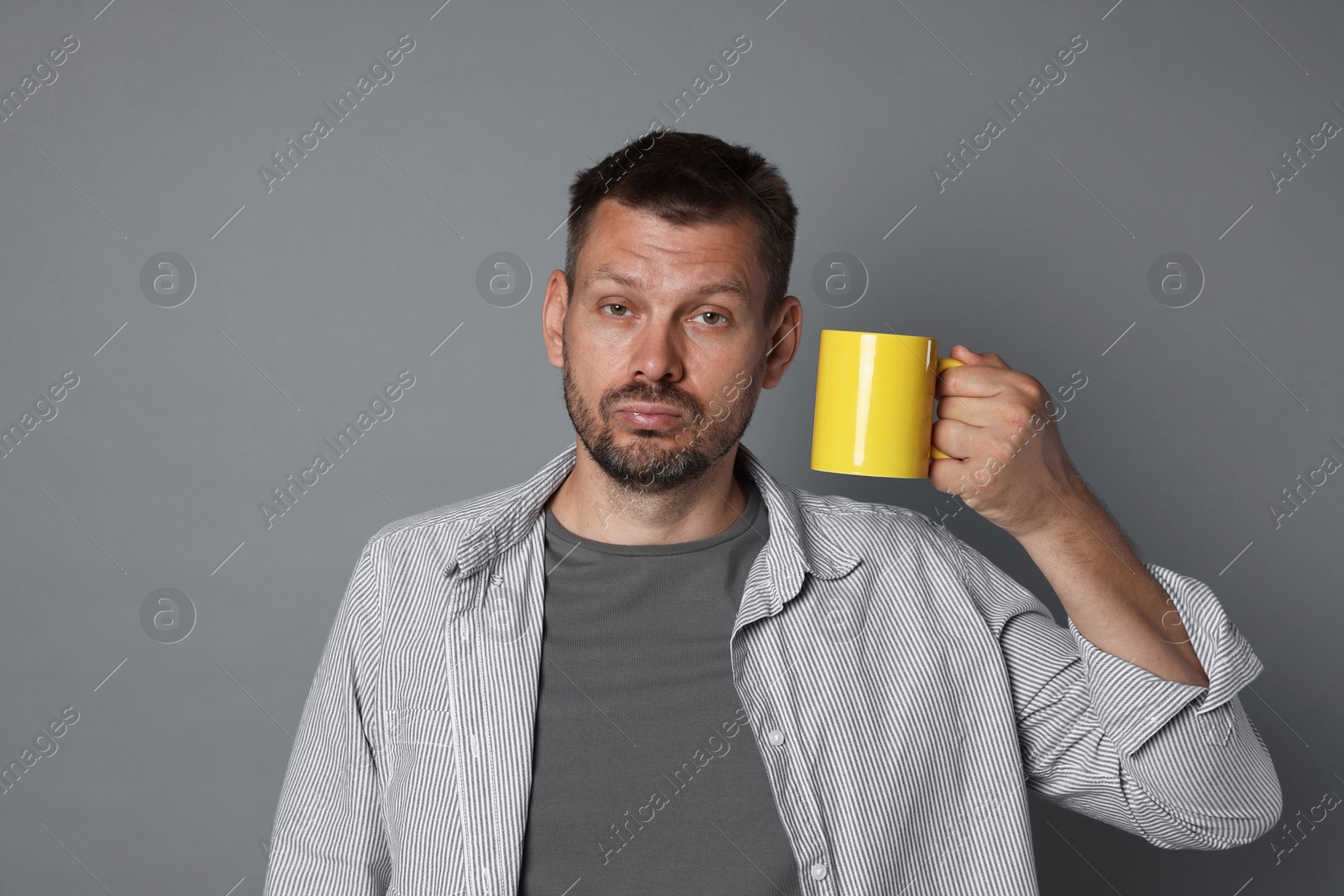 Photo of Man with cup of drink suffering from hangover on grey background