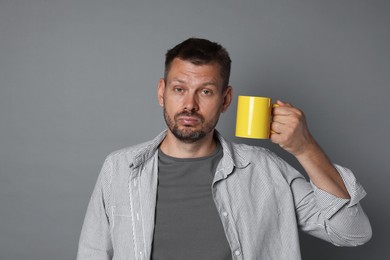 Photo of Man with cup of drink suffering from hangover on grey background