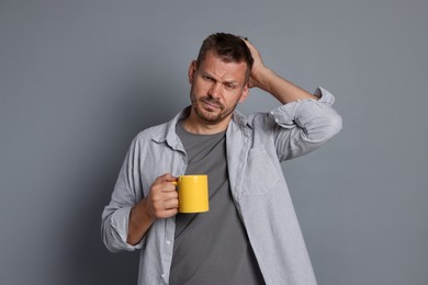 Photo of Man with cup of drink suffering from hangover on grey background