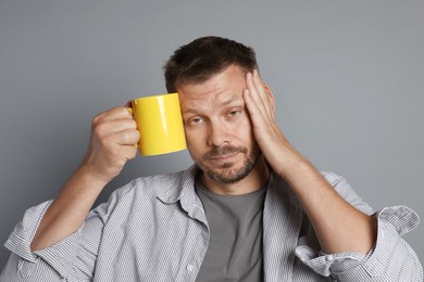Photo of Man with cup of drink suffering from hangover on grey background