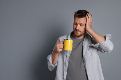 Photo of Man with cup of drink suffering from hangover on grey background, space for text