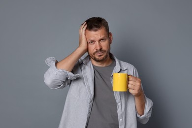 Photo of Man with cup of drink suffering from hangover on grey background
