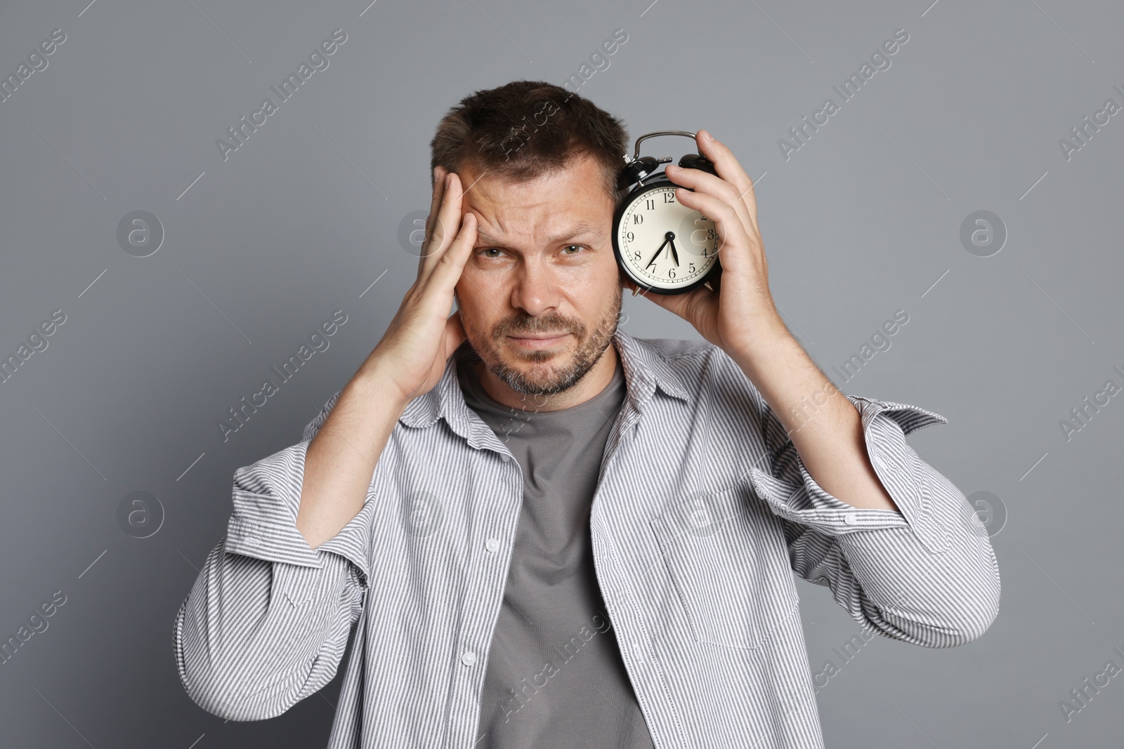 Man with alarm clock suffering from hangover on grey background Photo of Man with alarm clock suffering from hangover on grey background