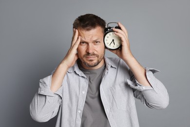 Photo of Man with alarm clock suffering from hangover on grey background
