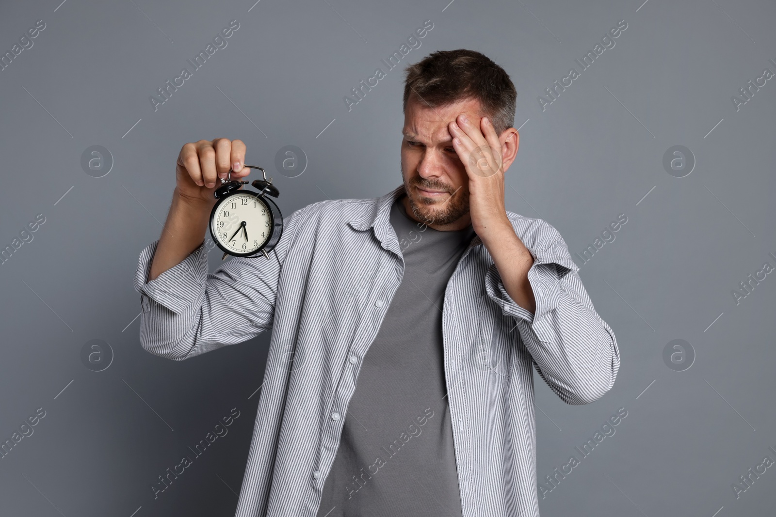 Man with alarm clock suffering from hangover on grey background Photo of Man with alarm clock suffering from hangover on grey background