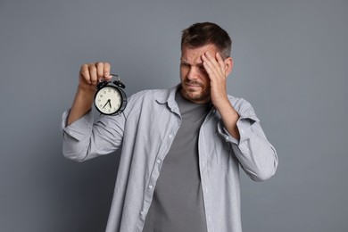 Photo of Man with alarm clock suffering from hangover on grey background