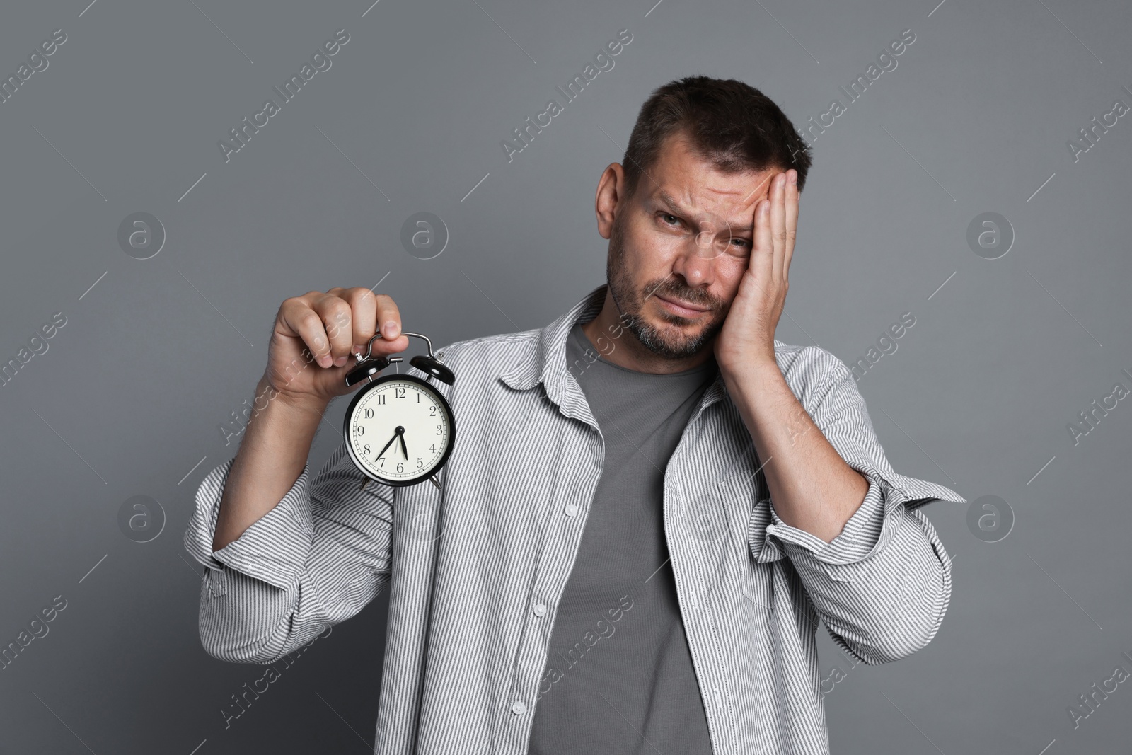 Man with alarm clock suffering from hangover on grey background Photo of Man with alarm clock suffering from hangover on grey background