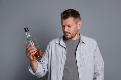 Photo of Man with bottle of whiskey suffering from hangover on grey background