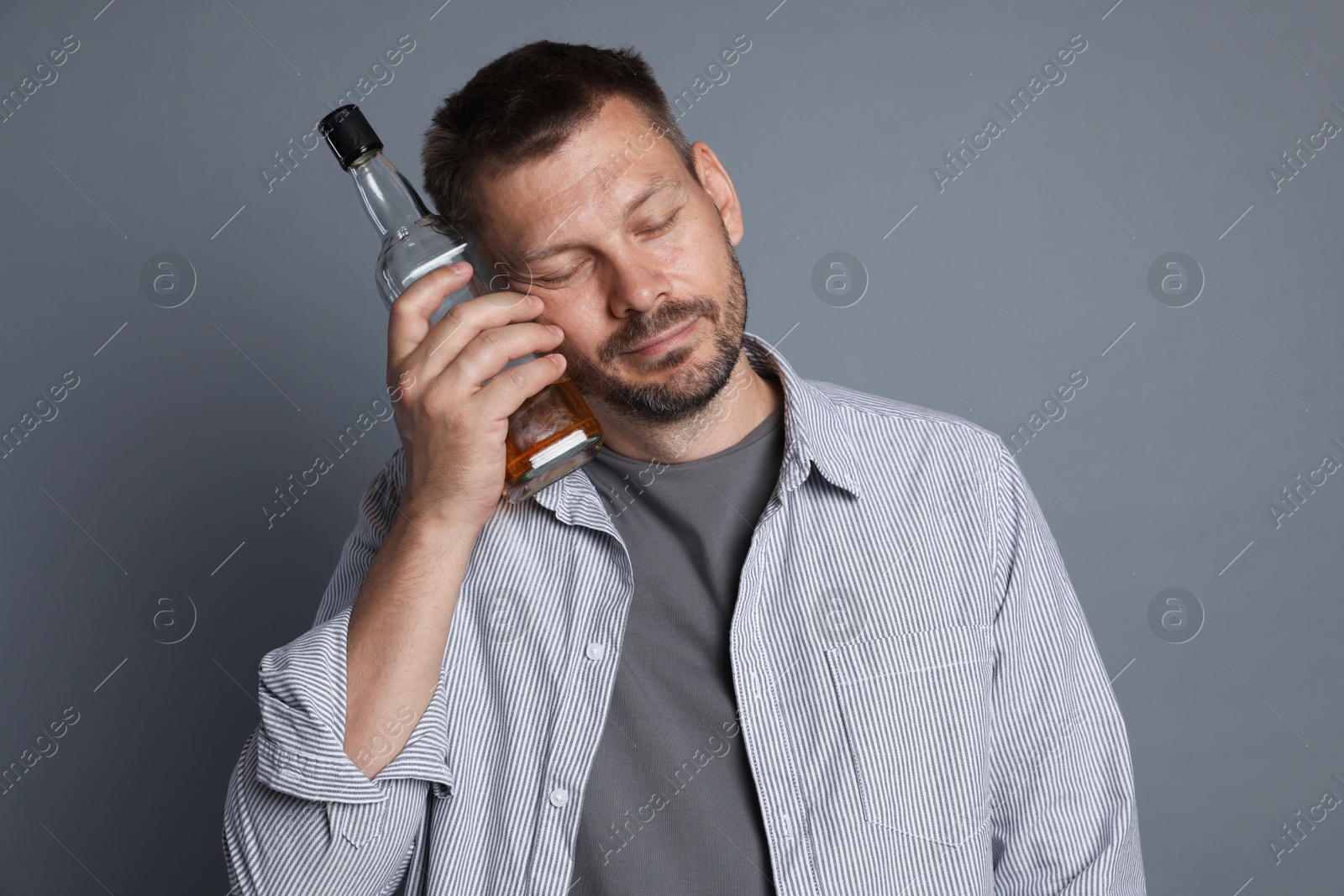 Photo of Man with bottle of whiskey suffering from hangover on grey background