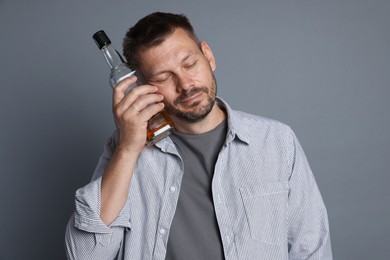 Photo of Man with bottle of whiskey suffering from hangover on grey background