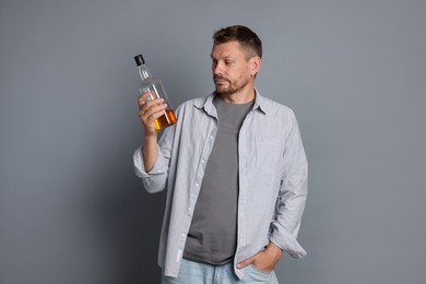Photo of Man with bottle of whiskey suffering from hangover on grey background