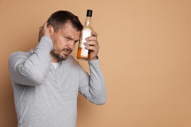 Photo of Man with bottle of whiskey suffering from hangover on beige background, space for text