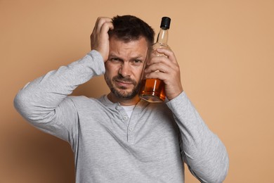 Photo of Man with bottle of whiskey suffering from hangover on beige background