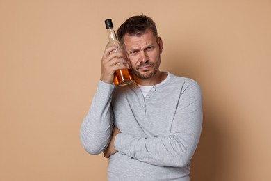 Photo of Man with bottle of whiskey suffering from hangover on beige background