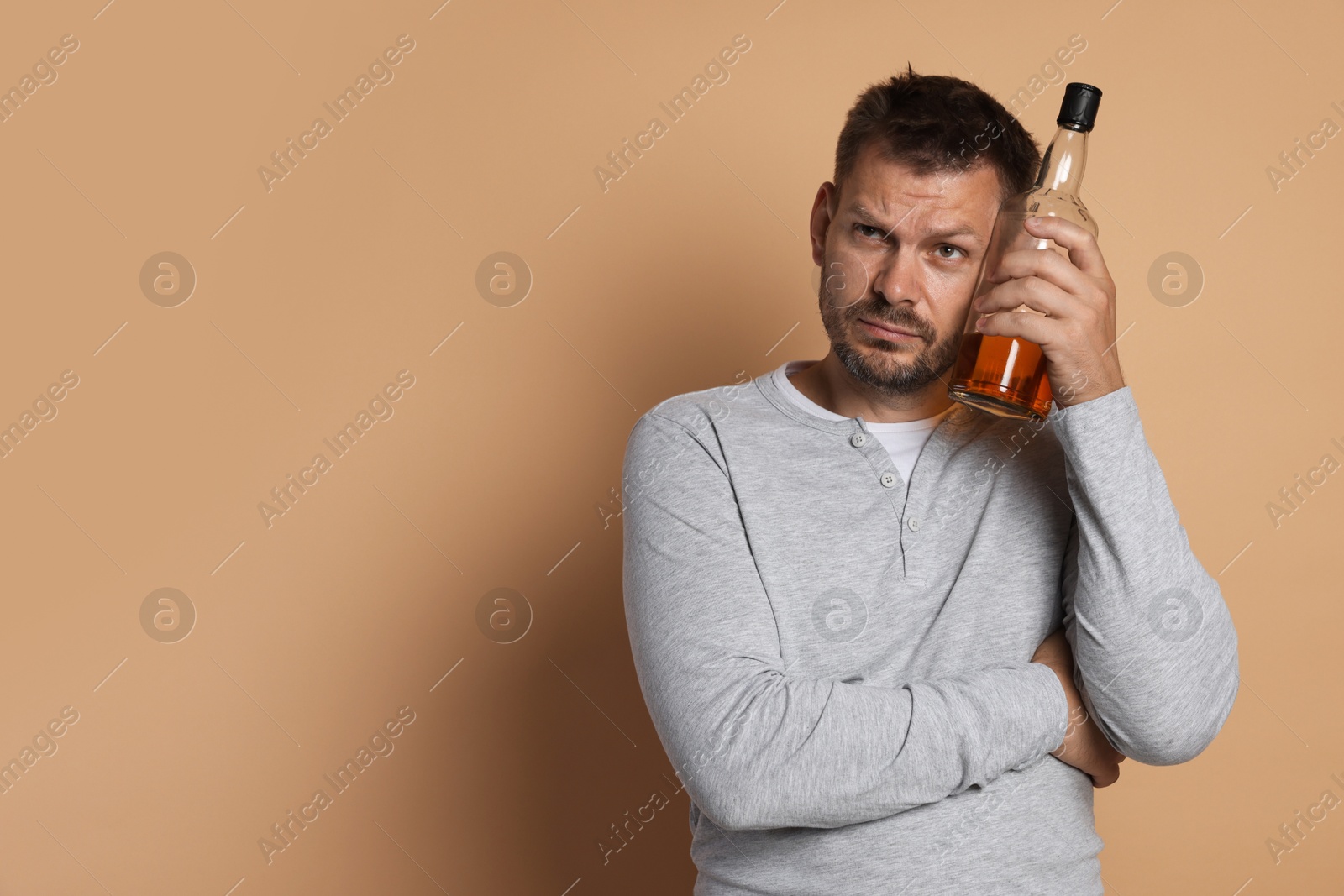 Photo of Man with bottle of whiskey suffering from hangover on beige background, space for text