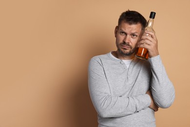 Photo of Man with bottle of whiskey suffering from hangover on beige background, space for text
