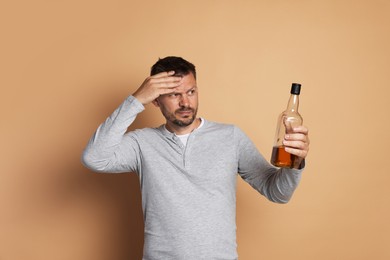 Photo of Man with bottle of whiskey suffering from hangover on beige background